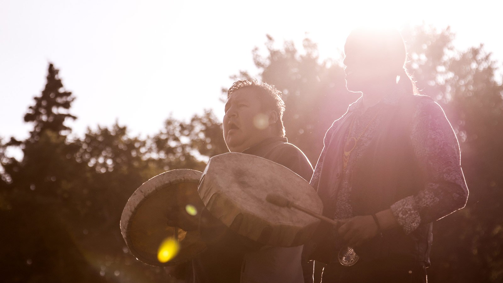 Two Indigenous men striking ceremonial drums